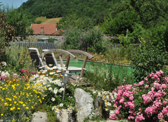Vue sur la piscine naturelle et écologique de la chambre d'hôtes avec au premier plan un petit massif fleuri et un petit pont de bois